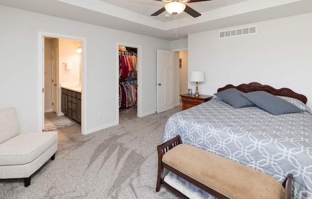 bedroom with a spacious closet, visible vents, baseboards, a tray ceiling, and light carpet