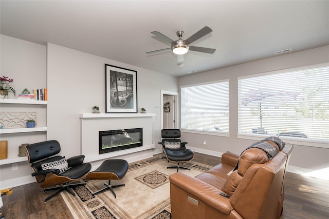 living room featuring visible vents, baseboards, wood finished floors, a glass covered fireplace, and a ceiling fan