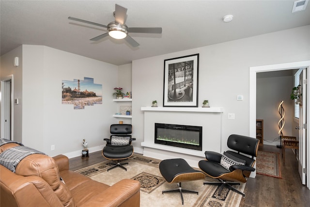 living area featuring visible vents, a ceiling fan, a glass covered fireplace, wood finished floors, and baseboards