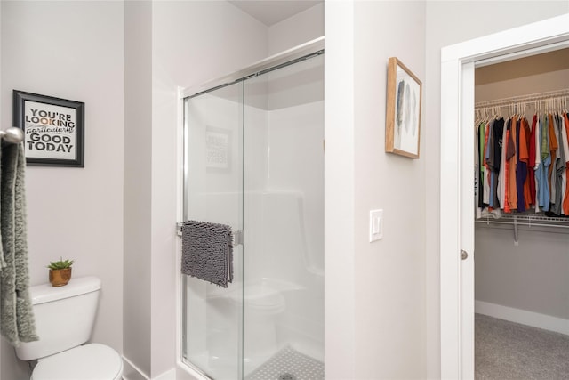 bathroom featuring baseboards, toilet, a stall shower, and a spacious closet