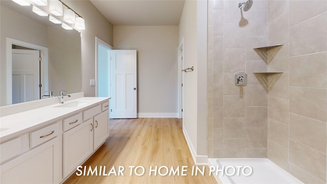 bathroom featuring wood finished floors, tiled shower, double vanity, and a sink