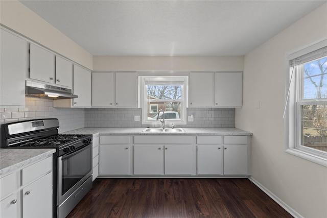 kitchen featuring dark wood finished floors, a sink, under cabinet range hood, stainless steel gas range oven, and backsplash