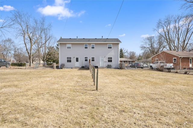 rear view of house with central AC unit, fence, and a lawn