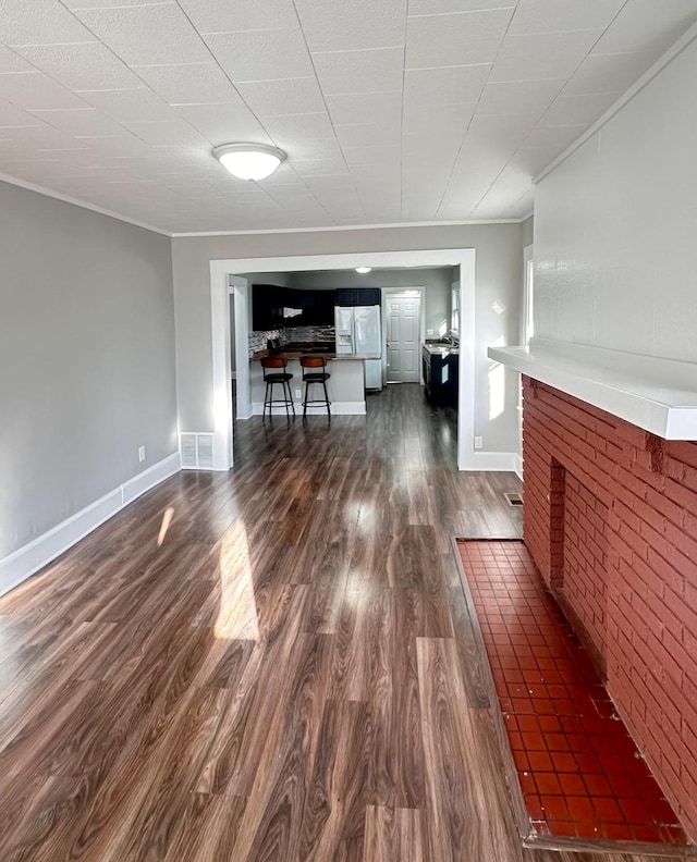 unfurnished living room featuring visible vents, ornamental molding, dark wood-style floors, baseboards, and a brick fireplace