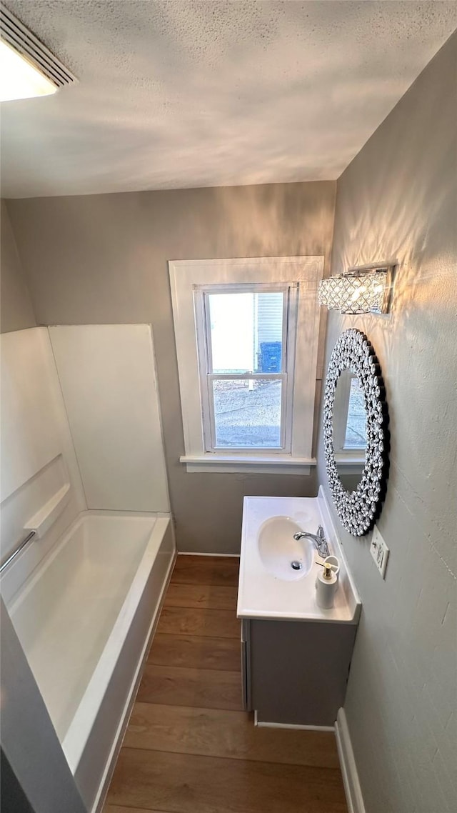 full bath featuring visible vents, a tub, vanity, wood finished floors, and a textured ceiling