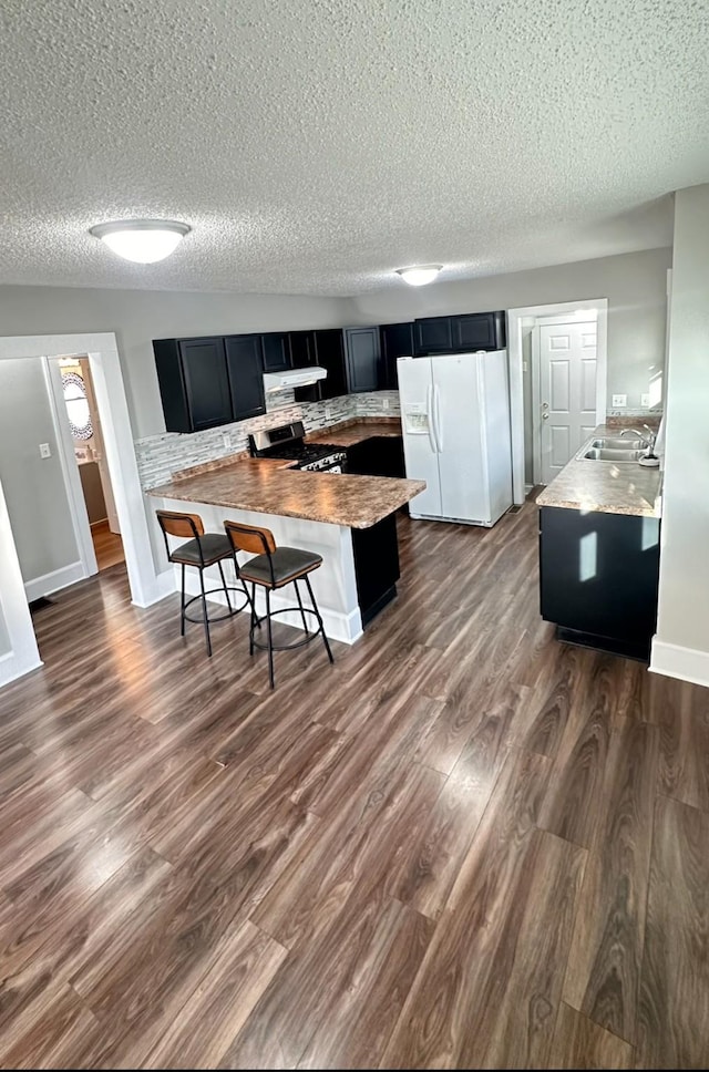 kitchen with a sink, dark wood-style floors, white fridge with ice dispenser, stainless steel range with gas cooktop, and a breakfast bar area