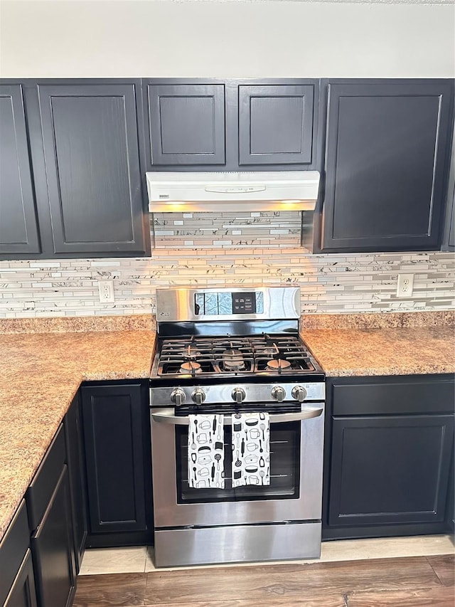 kitchen with under cabinet range hood, gas stove, tasteful backsplash, and light wood-type flooring