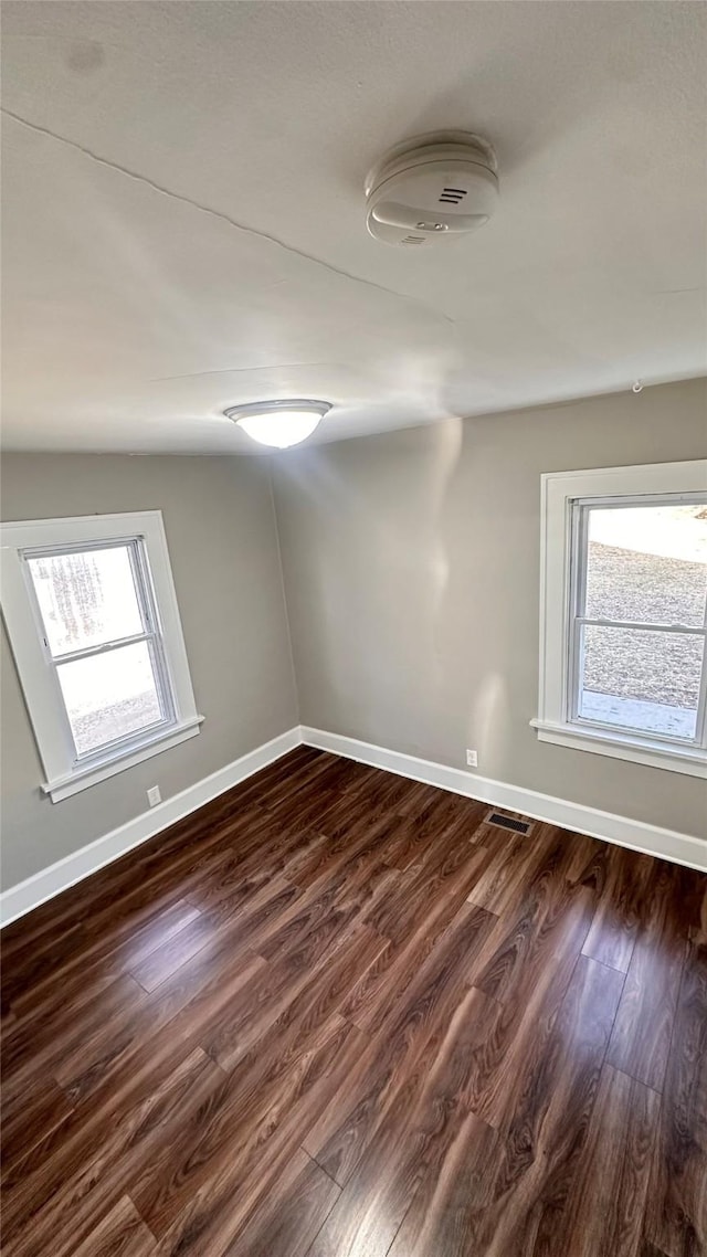 spare room featuring visible vents, baseboards, and dark wood-style flooring