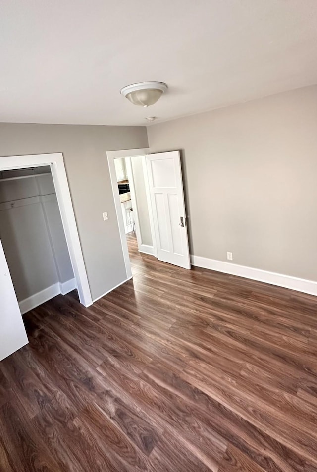 unfurnished bedroom with a closet, baseboards, and dark wood-type flooring