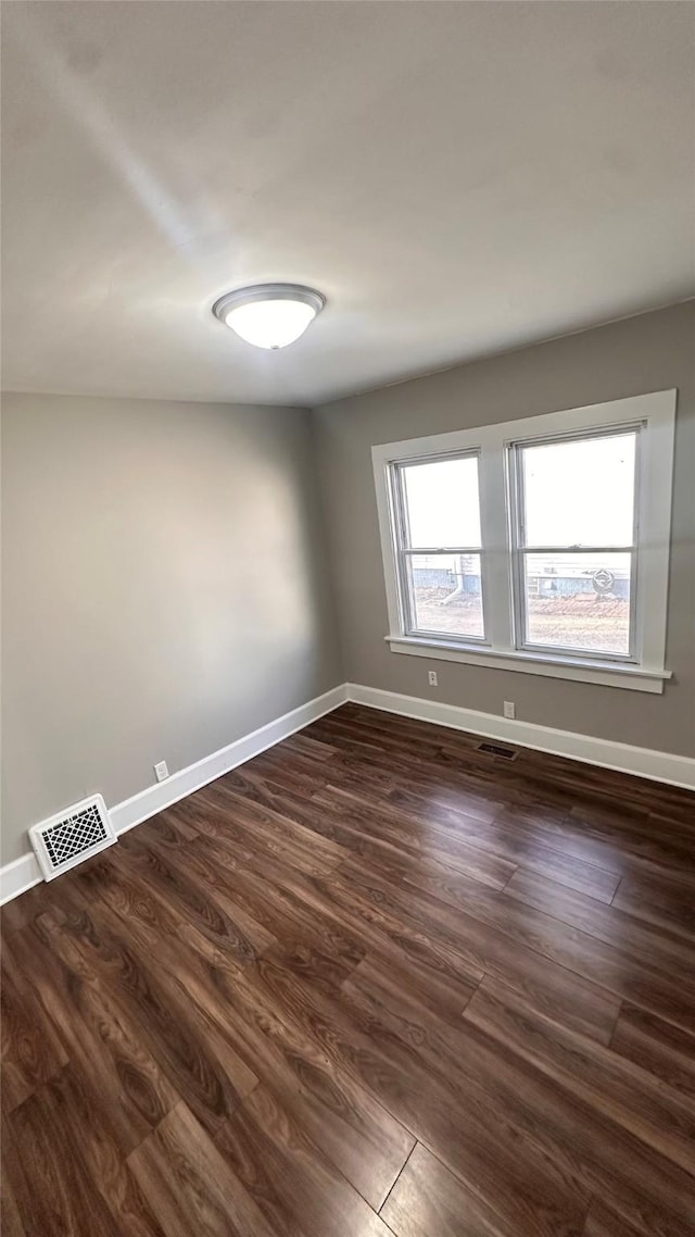 spare room with visible vents, baseboards, and dark wood-style floors