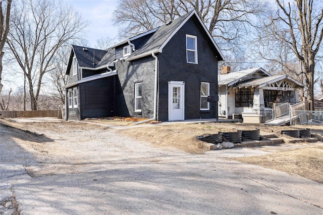 view of side of property featuring stucco siding, a shingled roof, and fence