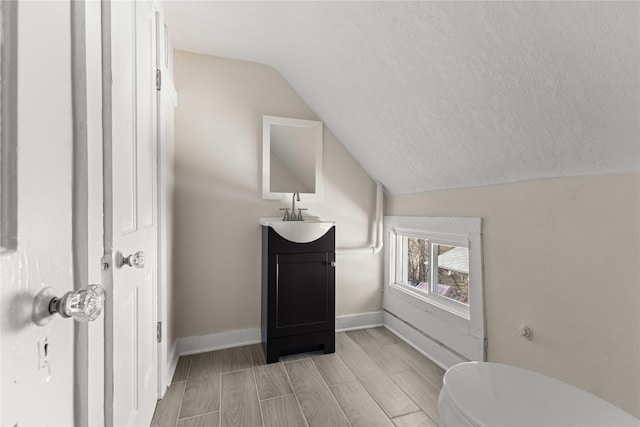 bathroom with vanity, baseboards, lofted ceiling, a textured ceiling, and toilet