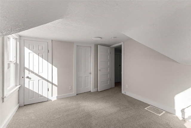 bonus room featuring baseboards, visible vents, carpet floors, and a textured ceiling