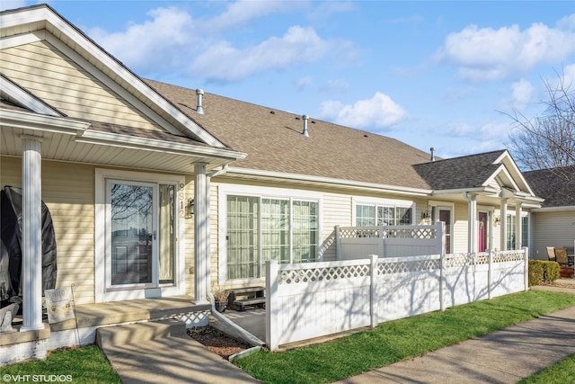 back of property with fence, covered porch, and a shingled roof