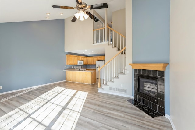 unfurnished living room featuring light wood-type flooring, visible vents, baseboards, ceiling fan, and stairs