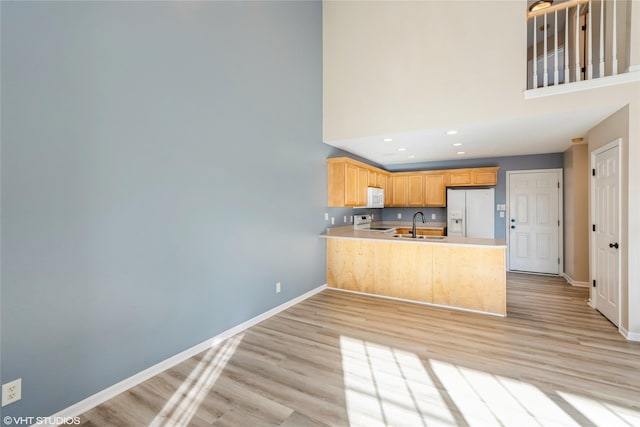 kitchen with white appliances, baseboards, light wood finished floors, a peninsula, and a towering ceiling