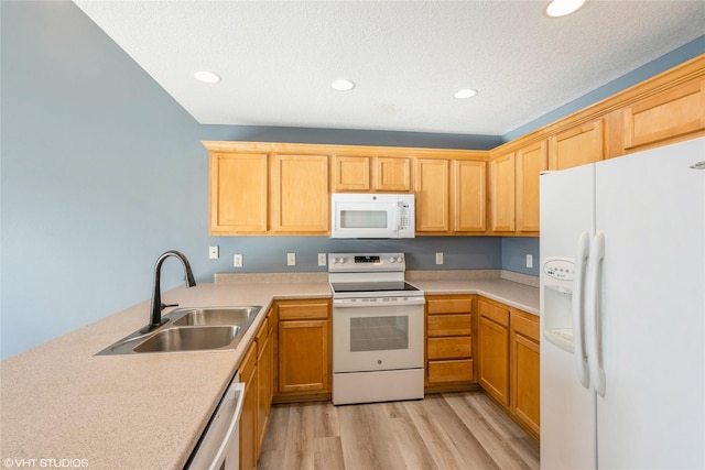 kitchen with white appliances, a peninsula, a sink, light countertops, and light wood-type flooring