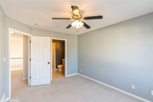 unfurnished bedroom with baseboards, light colored carpet, ensuite bath, and a ceiling fan