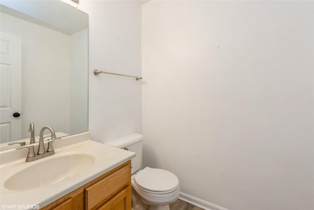 half bathroom featuring toilet, vanity, and baseboards