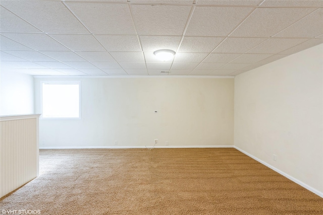 carpeted empty room featuring a drop ceiling and baseboards