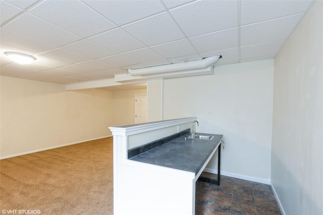 unfurnished office featuring a sink, a paneled ceiling, baseboards, and dark carpet