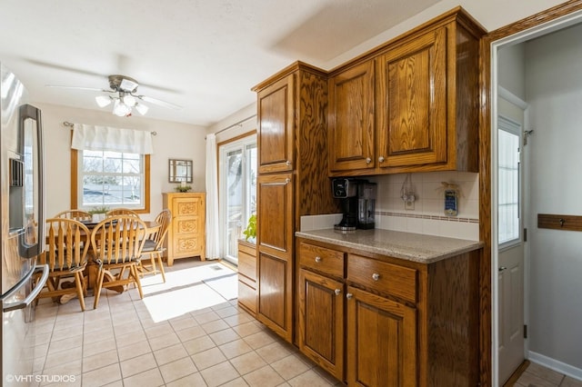 kitchen with a ceiling fan, brown cabinetry, light tile patterned flooring, stainless steel fridge with ice dispenser, and backsplash