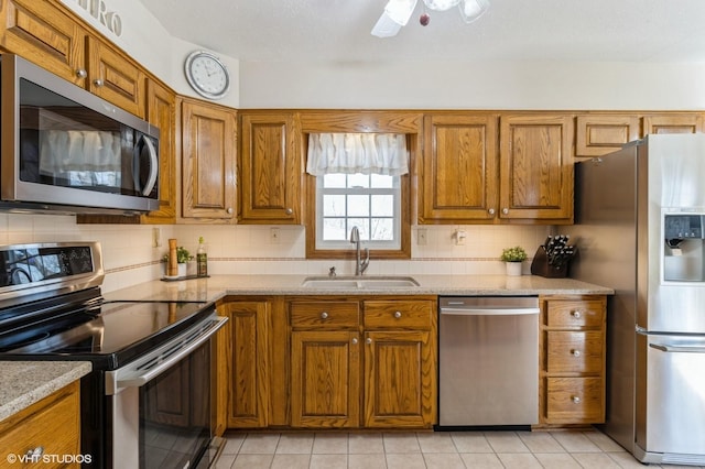 kitchen featuring light tile patterned floors, decorative backsplash, appliances with stainless steel finishes, brown cabinetry, and a sink