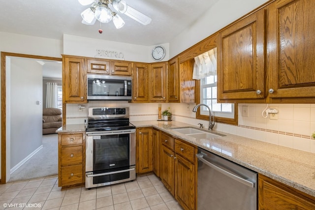 kitchen with ceiling fan, light stone countertops, brown cabinets, stainless steel appliances, and a sink