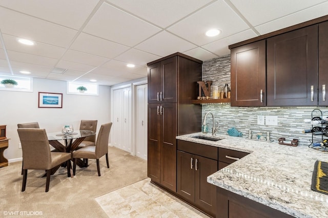 kitchen with open shelves, a sink, tasteful backsplash, dark brown cabinetry, and light colored carpet