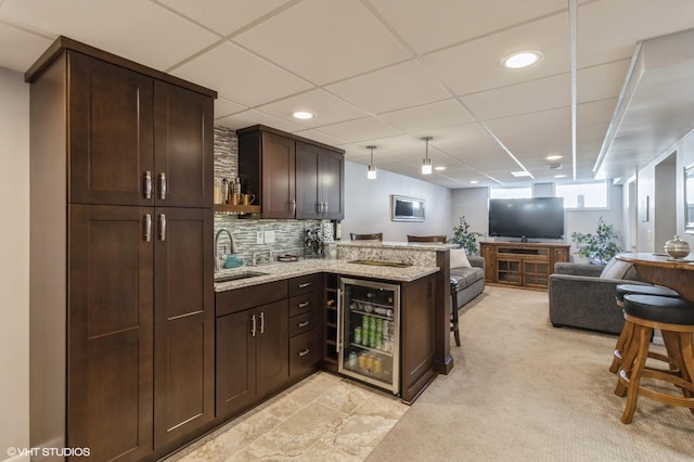 kitchen with a peninsula, a sink, wine cooler, dark brown cabinets, and open floor plan