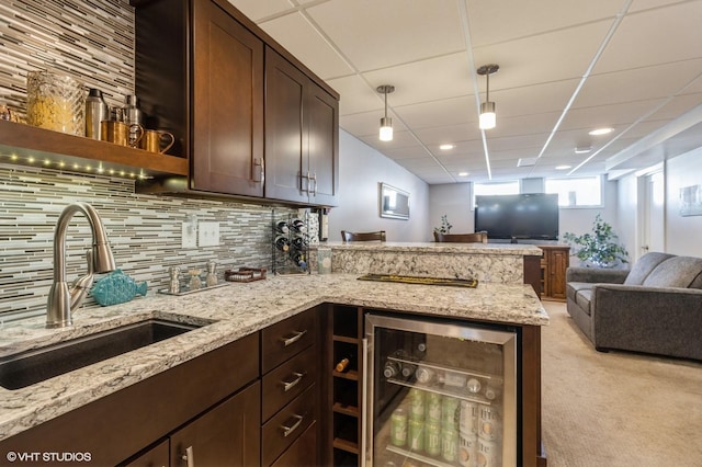 kitchen with dark brown cabinets, backsplash, wine cooler, open floor plan, and a sink