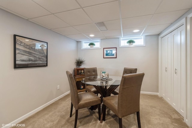 dining area featuring light colored carpet, a paneled ceiling, and baseboards