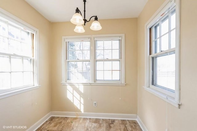 unfurnished dining area featuring a wealth of natural light, baseboards, and an inviting chandelier