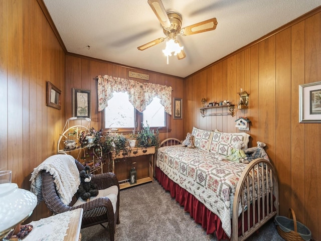 carpeted bedroom with a textured ceiling, a ceiling fan, wood walls, and ornamental molding