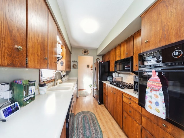 kitchen featuring black appliances, a sink, backsplash, light wood finished floors, and light countertops