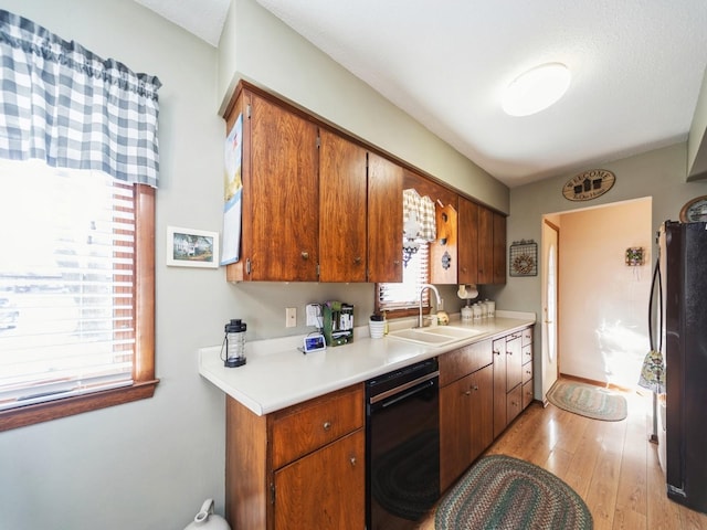 kitchen with light countertops, light wood-style flooring, brown cabinetry, black appliances, and a sink