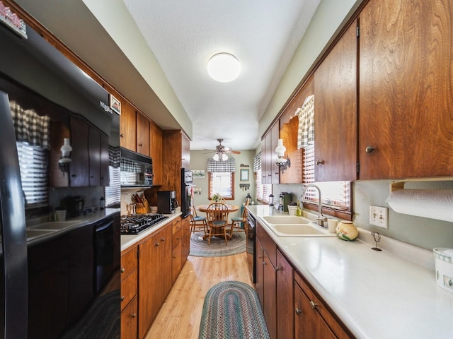 kitchen featuring a sink, black appliances, light countertops, light wood-style floors, and brown cabinets