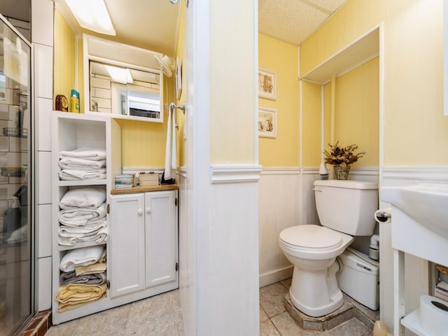 full bathroom with a shower stall, toilet, a wainscoted wall, and tile patterned floors