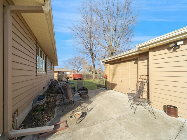 view of patio with a garage, fence, concrete driveway, and an outdoor fire pit