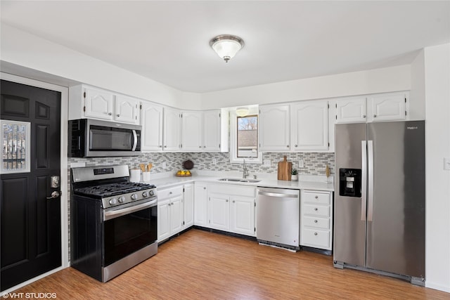 kitchen with a sink, appliances with stainless steel finishes, white cabinets, and light wood finished floors