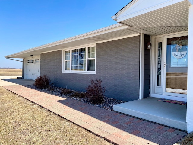 doorway to property featuring concrete driveway, a garage, and brick siding