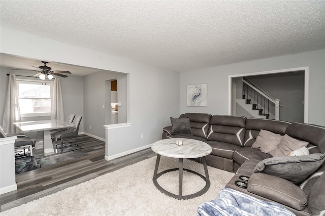 living area with stairway, a textured ceiling, baseboards, and wood finished floors