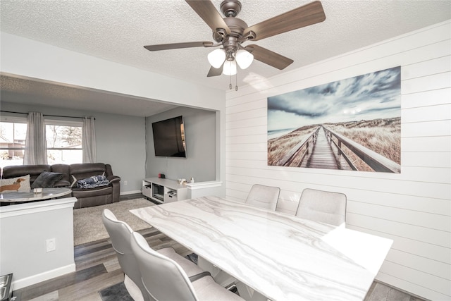 dining space with wood walls, a textured ceiling, a ceiling fan, and wood finished floors