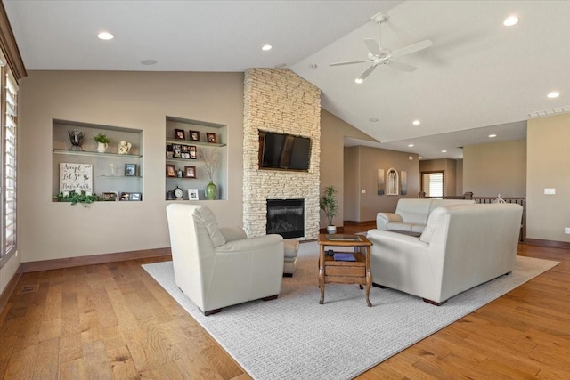 living room featuring light wood finished floors, visible vents, ceiling fan, built in features, and a stone fireplace