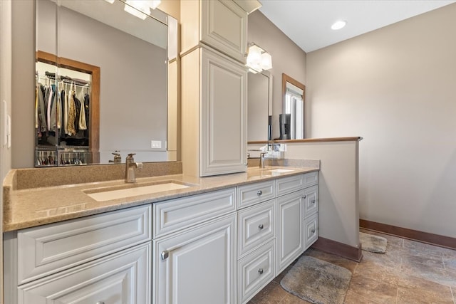 full bath with baseboards, double vanity, recessed lighting, a sink, and stone finish flooring