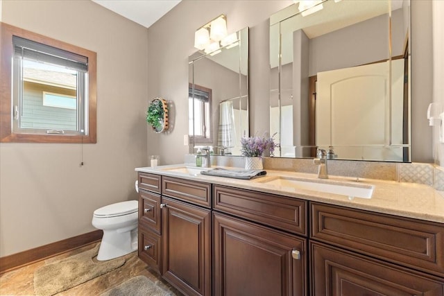 full bath featuring double vanity, toilet, baseboards, and a sink