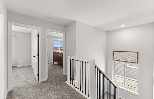 hallway with an upstairs landing, baseboards, and carpet floors