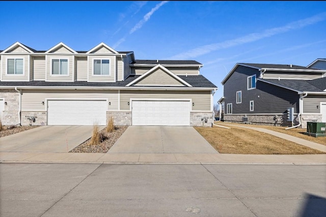 townhome / multi-family property featuring stone siding, central AC, and concrete driveway