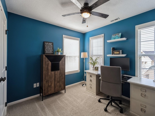 office featuring visible vents, a ceiling fan, a textured ceiling, baseboards, and light colored carpet