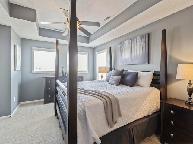 bedroom with visible vents, light carpet, a tray ceiling, baseboards, and ceiling fan